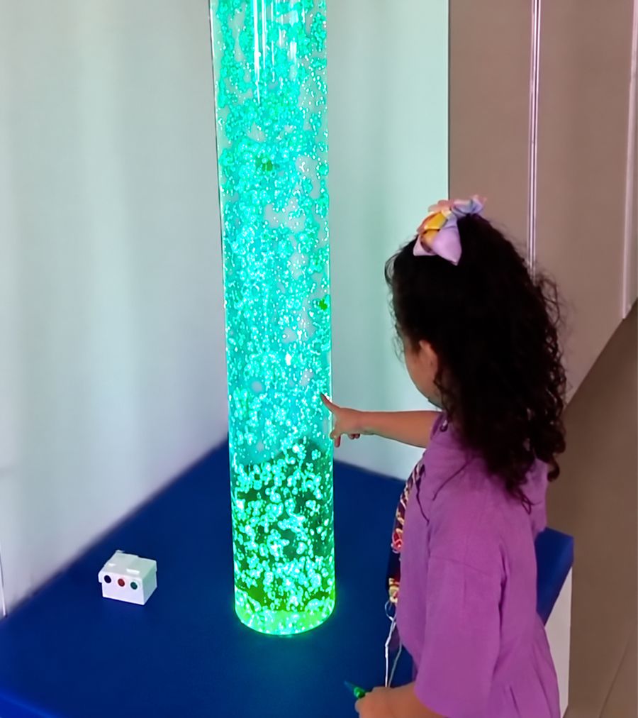 Criança interagindo com coluna de bolhas em sala multissensorial
